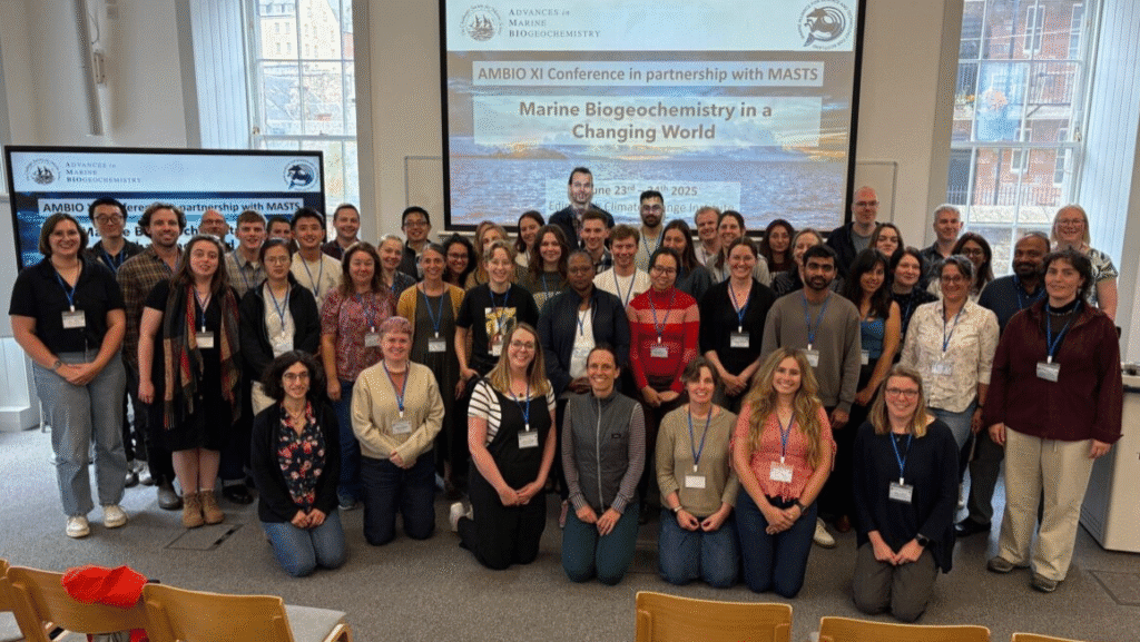 Group of conference attendees smiling at the camera surrounded by large Power Point screens